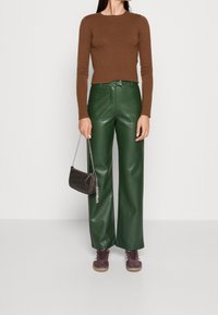 Brązowa bluzka z długim rękawem, zielone skórzane spodnie o szerokich nogawkach, fioletowe trampki i mała ciemna torebka na łańcuszku.