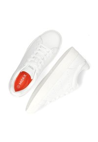 Zapatillas blancas con parte superior de cuero texturizado, punta redonda y diseño con cordones. La plantilla roja lleva el logotipo "MCXX". Estilo minimalista, sin patrones visibles.