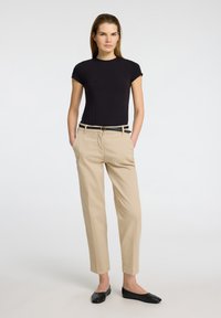 Černé přiléhavé tričko, béžové kalhoty na míru s černým opaskem a zlatou sponou, a černé baleríny. Tento outfit se vyznačuje minimalistickým stylem.