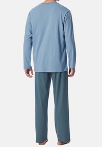 Camisa de manga larga azul claro combinada con pantalones de pijama oscuros con estampado, que presentan un corte holgado y una textura suave.
