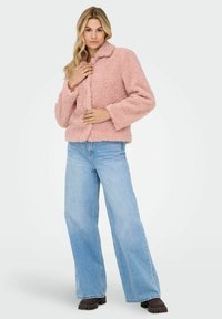 Blush pink faux fur jacket with a collar, front button closure, and wide sleeves, paired with light blue wide-leg jeans and dark shoes.