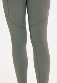 Olijfgroene, high-waisted leggings van rekbaar materiaal met stiksel details en geperforeerde accenten op het bovenbeen.