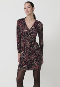 Vestido negro ajustado con mangas largas, que presenta un patrón paisley en rojo y dorado, hecho de una tela suave y elástica.