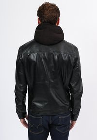 Černá kožená bunda s odepínací černou kapucí, s hladkým povrchem, přiléhavým střihem a detailním prošíváním podél ramen.