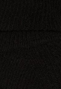 Zbliżenie czarnej dzianiny z widoczną prążkowaną teksturą i poziomym szwem na środku.