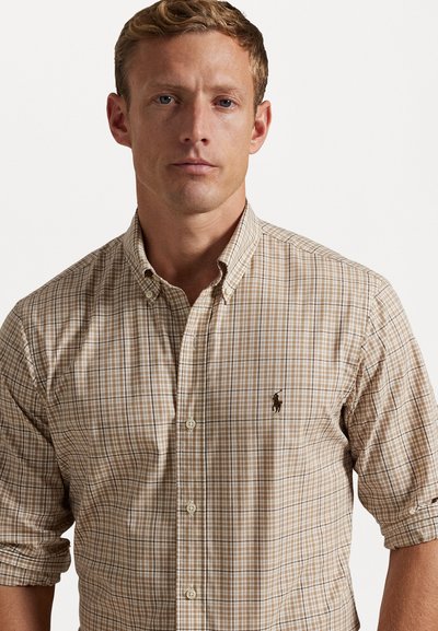 Chemise à carreaux marron à boutons avec un col classique, des manches retroussables et un petit logo brodé sur le côté gauche de la poitrine.
