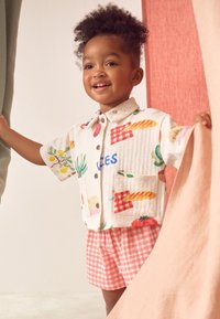Short-sleeved, multicolored shirt with food-themed patterns, beige background, and two pockets, paired with pink gingham shorts.