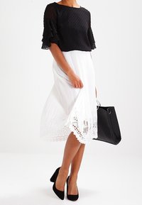 Top corto a pois neri, gonna midi bianca plissettata con orlo in pizzo. Tacchi alti neri e una borsa a tracolla nera completano l'outfit.