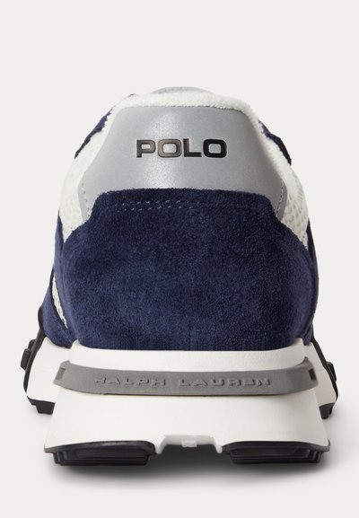 Гледка отзад на маратонка в тъмносиньо и бяло с "POLO" на задната част и "RALPH LAUREN" отпечатано на сивата средна част на подметката.