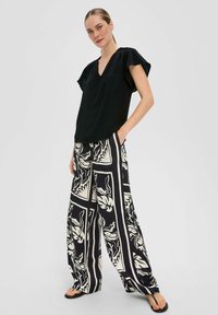 Zwarte V-hals blouse met korte vlinder mouwen, gecombineerd met wijde broek in een zwart-wit bloemenpatroon.