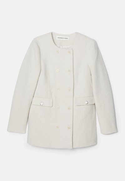 Casaco branco de duas fileiras com um tecido texturizado, gola redonda e dois bolsos frontais, apresentando detalhes decorativos em botões.