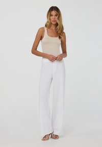 Top aderente beige abbinato a pantaloni bianchi larghi e svasati. Modella indossa sandali color beige, con capelli lisci e ondulati.