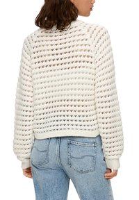 Häkelstrick weißer Pullover mit lockerer Passform, der offene Struktur und gerippte Bündchen aufweist. Kombiniert mit hoch sitzenden, hellblauen Jeans.