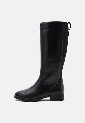 Botte haute en cuir noir avec petit talon, bout arrondi et panneau élastique à l'arrière pour un ajustement facile.