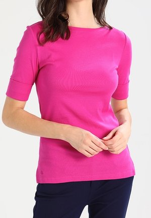 Haut fuchsia à manches courtes en tissu lisse avec un col rond, présentant une coupe ajustée et un design minimaliste, associé à un pantalon foncé.