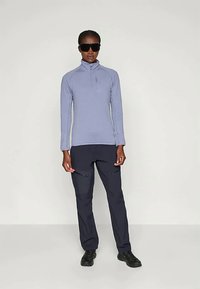 Svijetloplavi pulover dugih rukava sa ovratom na koji se može zakopčati, uparen s tamnoplavim hlačama s džepovima na patentni zatvarač i crnim cipelama.