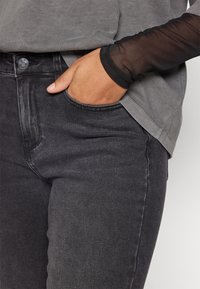 Vaqueros de mezclilla negra con un corte slim, que presentan un bolsillo delantero y una superposición gris de manga corta con detalles de mangas transparentes negras.