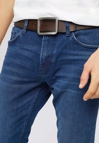Jeans en denim bleu foncé au design ajusté, complétés par une ceinture en cuir marron avec une boucle métallique carrée.