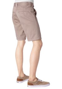 Pantaloni corti in cotone beige con taglio dritto, tasche laterali e dettaglio della tasca posteriore, abbinati a sneakers color cammello e bianche.