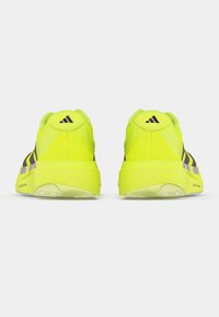 Helle gelbe Sportschuhe mit lila Akzenten, ausgestattet mit einem strukturierten Obermaterial, gepolsterten Sohlen und einem abgerundeten Rückendesign.