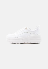 Άσπρο chunky αθλητικό παπούτσι με χοντρή σόλα, διακριτικές λεπτομέρειες ραφής, κορδόνια στο μπροστινό μέρος και λεπτομέρεια με λογότυπο στη φτέρνα, σε απλό φόντο.