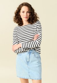 Gestreepte lange mouwen top in zwart en wit, gecombineerd met een lichtblauwe denim rok. De top heeft knoopaccenten op de mouwen.