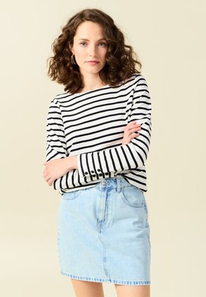 Gestreepte lange mouwen top in zwart en wit, gecombineerd met een lichtblauwe denim rok. De top heeft knoopaccenten op de mouwen.