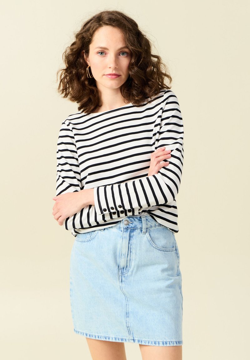 Gestreepte lange mouwen top in zwart en wit, gecombineerd met een lichtblauwe denim rok. De top heeft knoopaccenten op de mouwen.