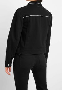 Black denim jacket with a fitted design, featuring a decorative silver accent across the upper back, and button cuffs. Simple and clean lines.