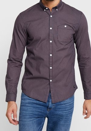 Chemise à boutons noire à motifs, avec une poche, présentant un petit motif géométrique blanc, des manches longues et un col à boutons.