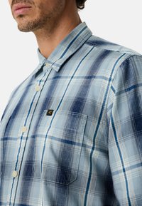 Blau kariertes Hemd mit Button-Down-Kragen, in verschiedenen Hell- und Dunkelblautönen. Mit Brusttasche und kleinem Logotag.