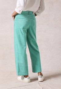 Mintgroene corduroybroek met een wijde pijp-design en achterzakken, gecombineerd met witte sneakers en een losvallend wit shirt.