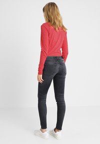 Vaqueros ajustados negros con un corte de talle medio y dos bolsillos traseros, combinados con una camiseta de manga larga a rayas rojas y blancas y zapatillas blancas.