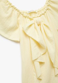 Gelbe schulterfreie Bluse aus strukturiertem Stoff, mit einem Rüschenausschnitt und einer Schleife auf der Vorderseite. Weiches, leichtes Material.