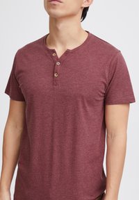 Camisa henley de manga corta en color marrón, hecha de una tela texturizada, con detalle de tres botones en el cuello.