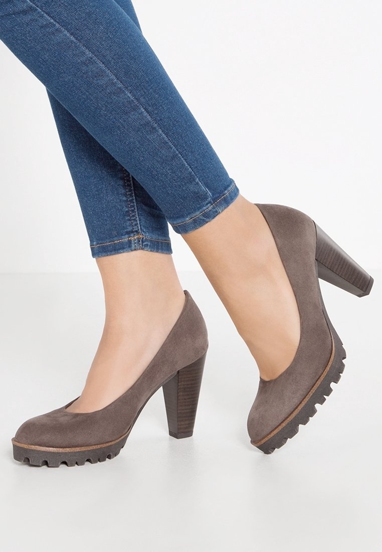 Zapatos de tacón alto de ante gris con punta redonda, que presentan una plataforma texturizada y un tacón de madera apilada, combinados con jeans ajustados azules.