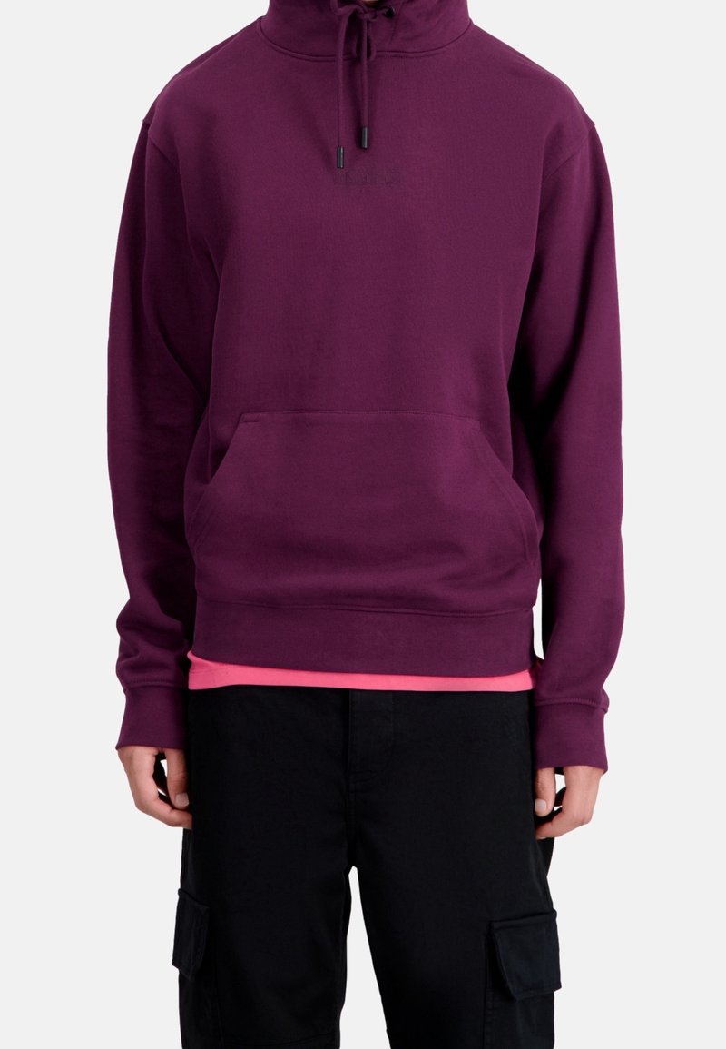 Sweat à capuche couleur violet profond avec une poche kangourou, un cordon à la capuche et des manches longues, porté sur un chemisier rose. Pantalon cargo noir visible.
