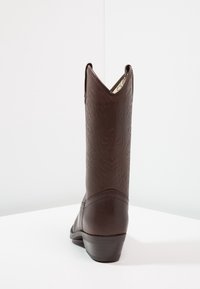 Botas de cowboy de cuero marrón con patrones decorativos en relieve, caña angular, punta ligeramente redondeada y un tacón bajo y apilado.