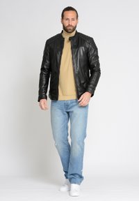 Sort læderjakke med quiltet skulderdetaljer, båret over en beige turtleneck, parret med lyseblå slidte jeans og hvide sneakers.