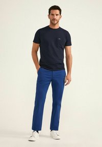 Camiseta de algodón azul marino con bolsillo, combinada con pantalones rectos azules y zapatillas blancas. Diseño sencillo, textura suave y acentos mínimos.