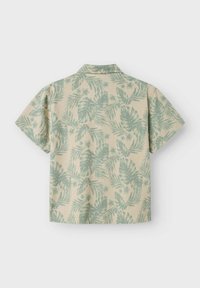 Camicia a maniche corte beige con motivo di foglie tropicali verdi. Presenta un colletto classico e una vestibilità rilassata. Tessuto morbido con finitura testurizzata.