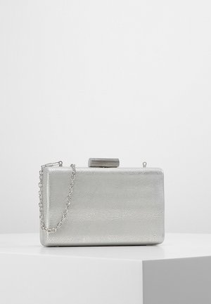 Pochette rectangulaire argentée avec motif texturé et bandoulière chaîne argentée, posée sur une surface blanche avec un fond clair uni.