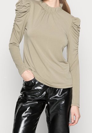 Lange mouwen, licht olijfgroene top met geplooide schouders en een gerimpelde halslijn, gecombineerd met glanzende zwarte kunstlederen broek.