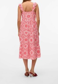 Czerwona i biała sukienka w wzory z falbaniastymi ramiączkami i warstwowym krojem, sięgająca do połowy łydki, noszona z czerwonymi sandałami na obcasie.