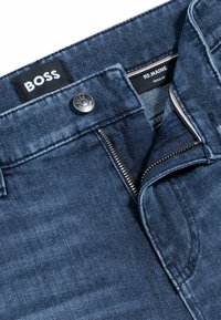 Dark blue denim jeans with a zip and button closure, featuring a "BOSS" label and contrasting inner lining. Regular fit with subtle texture.