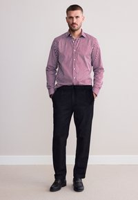 Hemd mit roten und weißen vertikalen Streifen, kombiniert mit lockeren schwarzen Hosen und schwarzen Schuhen. Einfaches Design, keine sichtbaren Muster.