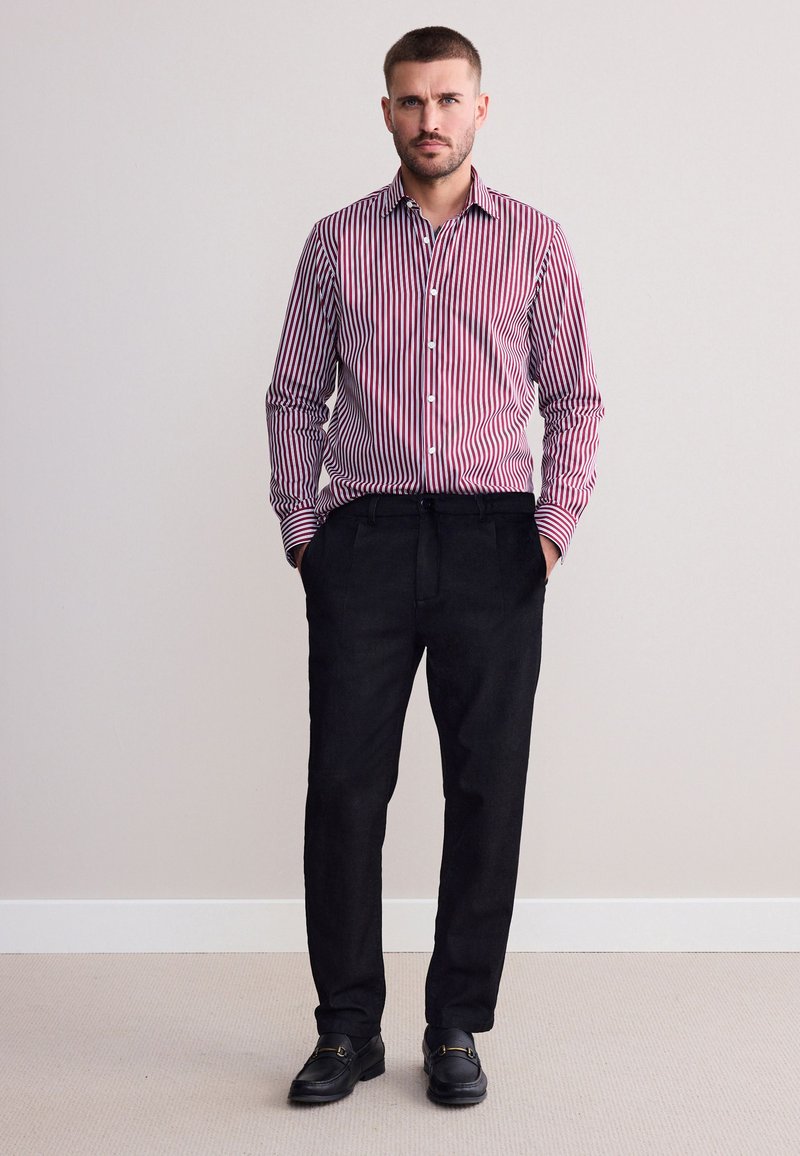 Hemd mit roten und weißen vertikalen Streifen, kombiniert mit lockeren schwarzen Hosen und schwarzen Schuhen. Einfaches Design, keine sichtbaren Muster.