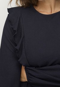 Granatowa, teksturowana bluzka z falbaniastymi rękawami i marszczonym materiałem w talii, z gładkim wykończeniem i miękką fakturą.