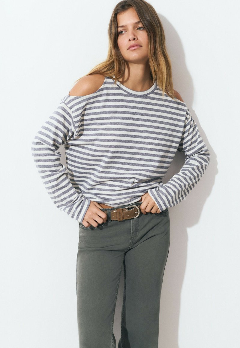 Striped long-sleeve sweater with cold-shoulder cutouts, in gray and white. Paired with olive green pants and a brown belt.