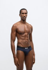 Chiloți din bumbac albastru marin cu o talie neagră care poartă logo-ul alb „BOSS”; textură fină și croială strânsă, concepuți pentru confort și susținere.